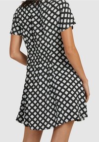 Robe noire à manches courtes avec un motif floral blanc, cintrée à la taille, et une jupe évasée qui tombe au-dessus du genou.