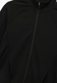 Schwarze Jacke aus weichem Stoff, mit einem durchgehenden Reißverschluss, hohem Kragen und schrägen Nähten für eine strukturierte Passform. Die strukturierte Oberfläche ist matt.