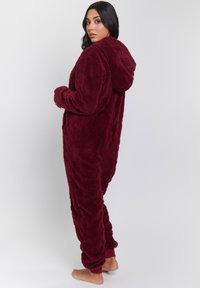 Pijama de terciopelo burdeos con un diseño de rombos, capucha y puños de canalé en los tobillos, que ofrece un ajuste suelto y cómodo para relajarse.