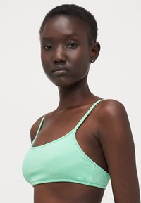 Bralette verde menta realizzato in tessuto testurizzato, con spalline sottili regolabili e una piccola etichetta del marchio sul lato. Superficie liscia.