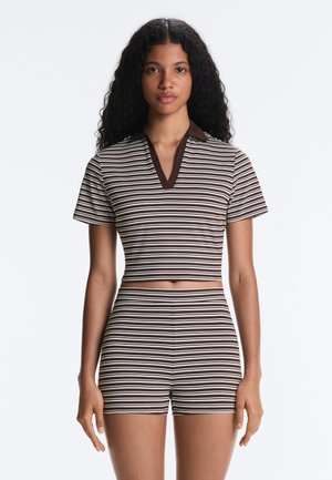 Kvinde med langt krøllet hår iført en brun og hvid horisontalt stribet kortærmet crop top og matchende shorts med høj talje.