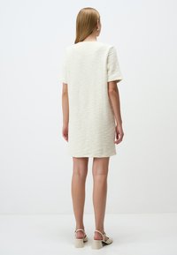 Vestito bianco corto a maniche corte con silhouette dritta, dotato di un semplice scollo rotondo e una lunghezza leggermente sopra il ginocchio.