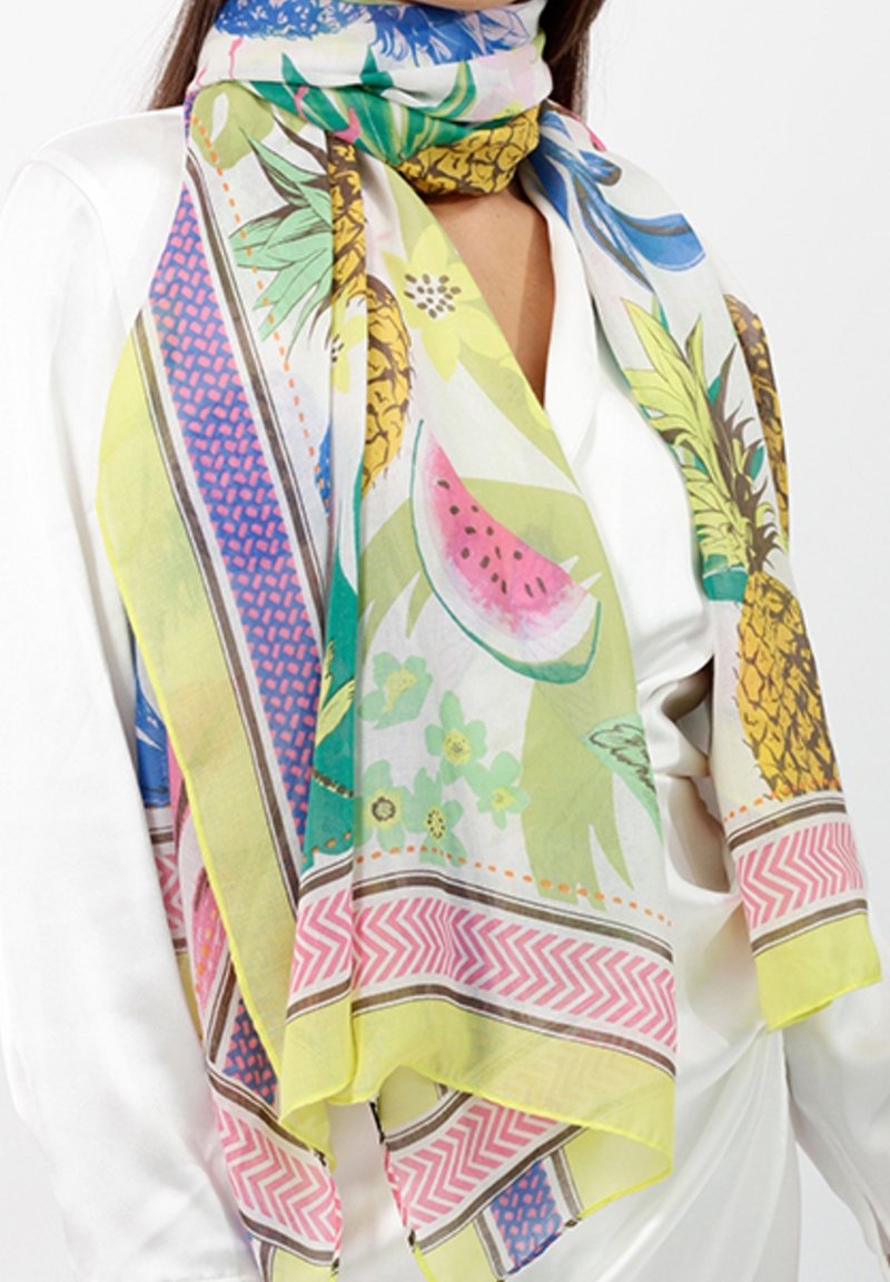 Femme portant une écharpe colorée avec des motifs d'ananas, de pastèque et de fleurs sur un chemisier blanc.