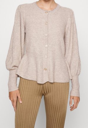 Cárdigan de punto color beige claro con mangas largas abullonadas y dobladillo acampanado, combinado con pantalones de talle alto de color marrón claro con pliegues.