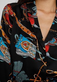 Černá halenka s barevným motivem koní, zahrnující živé červené, modré a složité vzory. Měkká tkanina, klasický límec a knoflíkové detaily.