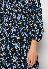 Robe noire avec imprimé floral bleu, tissu texturé, taille froncée et manches bouffantes. Présente une coupe décontractée et des fleurs de tailles variées.