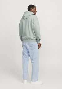 Felpa con cappuccio di colore verde chiaro dal fit rilassato, abbinata a jeans azzurri e sneakers bianche, vista da dietro.