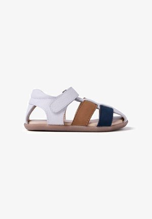 Sandalia infantil de punta abierta con correa blanca en el tobillo, tiras de cuero marrón y azul marino, y suela suave beige, mostrada en perfil lateral.