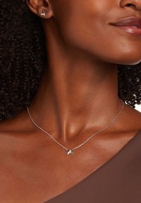 Zilveren vlinderketting met een delicate ketting, voorzien van een ingewikkeld vlinderontwerp. Model draagt een bruine top die de halslijn laat zien.