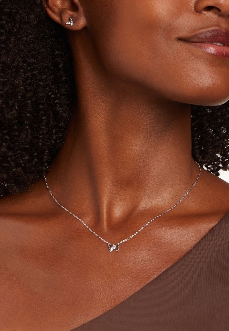 Zilveren vlinderketting met een delicate ketting, voorzien van een ingewikkeld vlinderontwerp. Model draagt een bruine top die de halslijn laat zien.