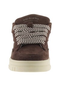 Sneaker in suede marrone con suola in gomma bianca, caratterizzato da un design testurizzato e lacci intrecciati marroni e bianchi. Logo sulla linguetta.