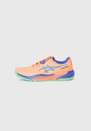 Tennisschuhe in Pfirsich mit blauen Akzenten und grüner Sohle. Sie verfügen über ein perforiertes Obermaterial für Atmungsaktivität und flache Schnürsenkel. Seitliches Logo sichtbar.