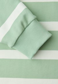 Tissu rayé horizontal vert clair et blanc avec une bordure côtelée repliée, montrant la texture et les détails du tricot.