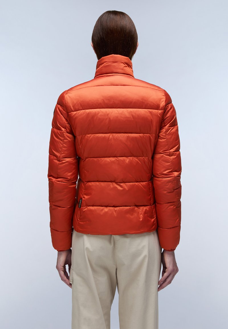 Giacca imbottita rossa con colletto alto, caratterizzata da cuciture orizzontali, tessuto liscio e lucido, e una vestibilità slim. Abbinata a pantaloni beige.