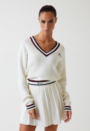 White v-neck sweater with red and green stripes at the neckline and cuffs, paired with a pleated white skirt featuring a striped waistband.