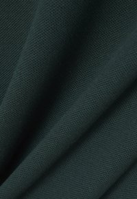 Donkergroen stof met een gestructureerde weving, met duidelijke plooien en kreukels die diepte en lagen in het materiaal creëren. Zacht aanvoelend.