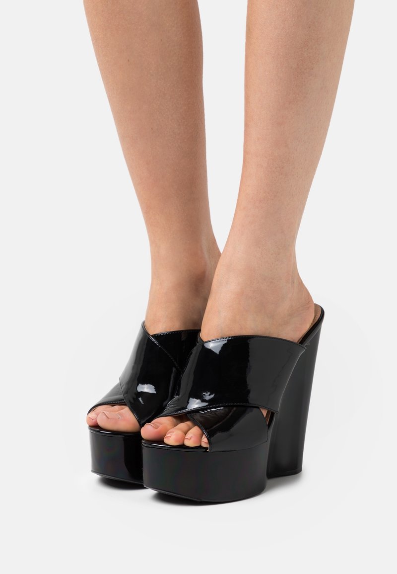 Mules compensées en cuir verni noir avec une large bride croisée et un bout ouvert, dotées d'un talon haut épais et d'une finition lisse.