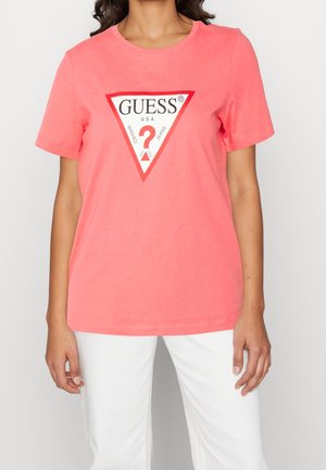 Korálově růžové bavlněné tričko s krátkým rukávem a kulatým výstřihem. Obsahuje červeno-bílé trojúhelníkové logo s textem "GUESS U.S.A.".