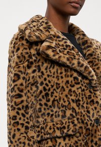 Kaput s imitacijom leopard uzorka od umjetnog krzna s rezanim ovratnikom, crnim gumbima i prednjim džepovima. Mekana tekstura, pretežno smeđa s tamnim mrljama.