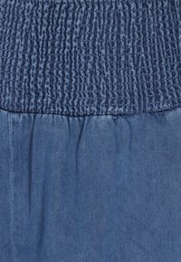 Kék farmer anyag smockolt gumis derékkal, amely texturált mintázatot és puha esést mutat.