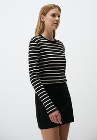 Camicia a maniche lunghe a righe bianche e nere con un design cropped, abbinata a una gonna nera uniforme. Tessuto morbido e vestibilità classica.