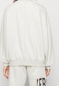 Felpa oversize grigio chiaro con spalle cadenti e orlo a costine, presenta una texture morbida e un minimo dettaglio delle cuciture.
