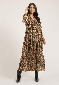 Robe longue à volants en tissu transparent présentant un motif de feuilles multicolores dans des tons de marron, or et rouge, avec une taille à nouer et des manches longues.
