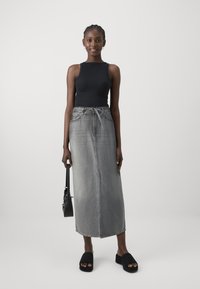 Svart tettsittende tanktopp, grå denim maxi skjørt med snøring og sidelåp, kombinert med svarte sandaler på plattform og en liten svart håndvott.