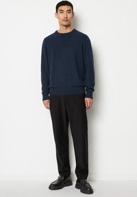 Marineblauer Strickpullover mit Rundhalsausschnitt, kombiniert mit schwarzen, maßgeschneiderten Hose und schwarzen Lederschuhen. Strukturiertes Material und gerippte Ärmelbündchen.