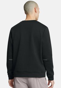 Zwarte sweatshirt met een ontspannen pasvorm, ronde halslijn en subtiele reflecterende accenten op de mouwen. Zachte textuur en minimalistisch ontwerp.