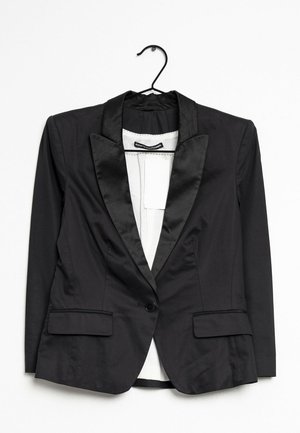 Blazer noir en satin avec revers, fermeture à un bouton et poches avant à rabat, suspendu sur un cintre noir sur fond blanc.
