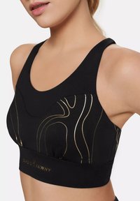 Schwarzer Sport-BH mit goldenem Wellenmuster; verfügt über einen breiten Bund mit Logo, breite Träger und eine glatte Textur. Entworfen für Komfort und Unterstützung.