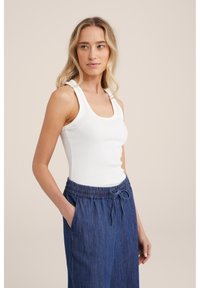 Hvid ribbet tanktop med en rund halsudskæring og brede stropper, parret med afslappede mørkeblå denimbukser med en elastisk talje.