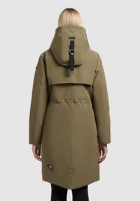 Olivgrüner Parka mit hohem Kragen, verstellbarer Kapuze und seitlichen Taschen. Verfügt über eine große Rückentasche und ein Logo-Patch nahe dem Saum.
