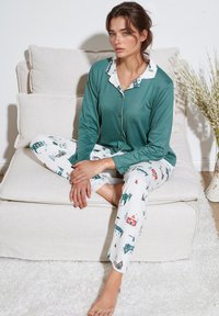 Zeleni button-up pidžama gornji dio sa bijelim hlačama s uzorkom kuća i drveća. Mekani materijal, opušteni kroj i dizajn ovratnika s kontrastnom bojom.