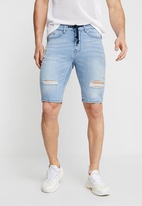 Shorts de mezclilla azul claro con un diseño desgastado, que presentan múltiples rasgaduras, una cinturilla con cordón ajustable y un ajuste slim.