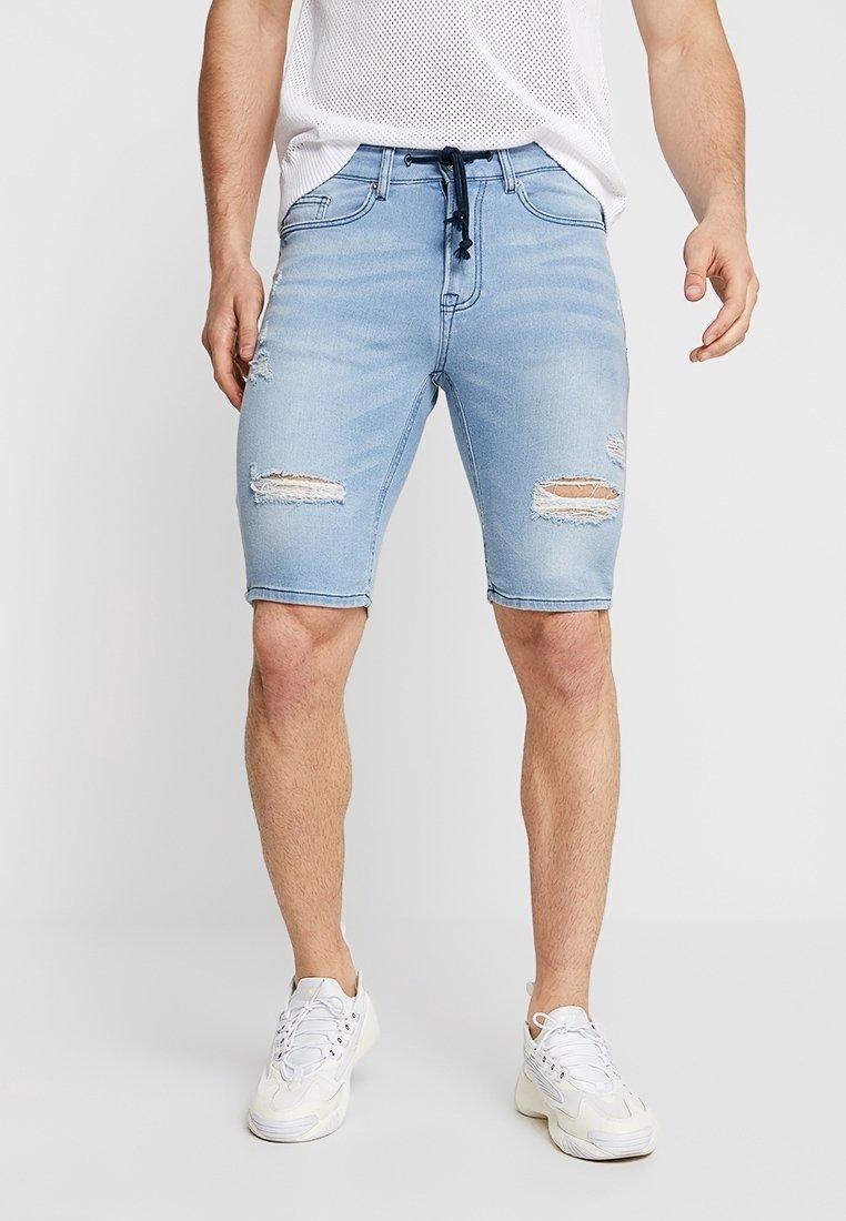 Shorts de mezclilla azul claro con un diseño desgastado, que presentan múltiples rasgaduras, una cinturilla con cordón ajustable y un ajuste slim.