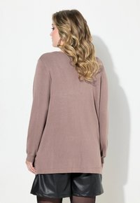 Pull à manches longues marron en texture côtelée, avec une coupe ample et un ourlet arrondi, associé à un short en cuir noir.