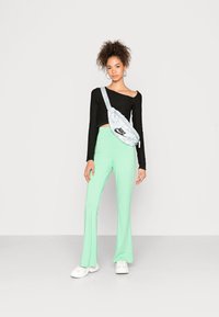 Top cropped preto de manga longa, calças flared verde menta claras e ténis brancos. Mala cruzada cinza em padrão camuflado com detalhe do logo preto.