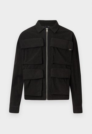 Black corduroy jacket with a zip closure, two large front pockets, and a collared neck. Simple design with ribbed texture and long sleeves.