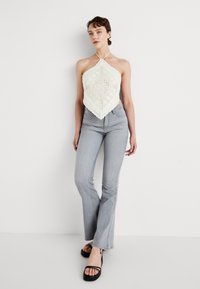 Top halter bianco all'uncinetto con motivo a diamante, abbinato a jeans grigi chiari a zampa d'elefante e sandali neri con cinturini. Tessuto morbido e design aderente.
