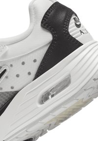Sapatilhas brancas e pretas com um superior em couro e malha, amortecimento de ar translúcido na sola e textura pontilhada nas laterais.