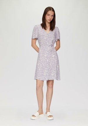 Lila Kleid mit floralem Muster, kurzen Ärmeln, V-Ausschnitt und Taillenschnüroption. Kombiniert mit weißen Plateausandalen. Glatte Stofftextur.