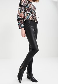 Mustat nahkaiset skinny-housut, jotka on yhdistetty kukkakuosiseseen puseroon, jossa on naru- ja mustan pitsin yksityiskohtia. Mallilla on jalassa teräväkärkiset korkokengät.