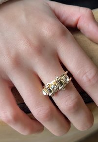 Gouden ring met sprankelende heldere stenen en ingewikkelde pareldetails. Het ontwerp omvat rechthoekige en ronde stenen in een gestructureerde band.
