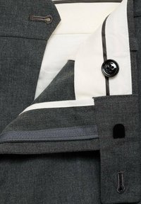 Interiorul unei jachete de costum gri, cu un căptușeală albă cu margine neagră, un singur buton negru și un buzunar lateral cu închidere cu fermoar.