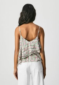 Top de tirantes con estampado floral en tejido ligero, que presenta volantes en capas, tirantes ajustables y una espalda en forma de V, combinado con pantalones blancos.