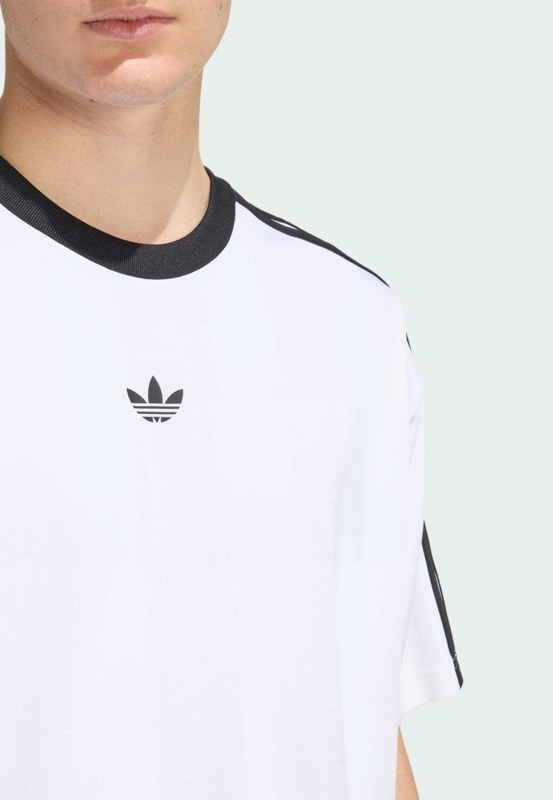 Camiseta blanca de Adidas con un cuello acanalado negro, rayas laterales negras y un pequeño logo negro en el pecho. Textura de tela suave.