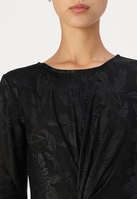 Vestido preto com texturas florais, decote redondo e detalhes franzidos na frente, feito de um tecido liso e leve.