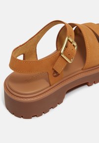 Hellbrauner Ledersandale mit breiten Riemen, verstellbarer goldener Schnalle und einer strukturierten braunen Plateau-Sohle mit Profilsohle.